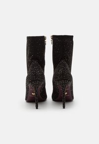 Botas de ante negras hasta el tobillo con punteras afiladas, decoradas con tachuelas plateadas, con cierre de cremallera y tacones de aguja delgados.