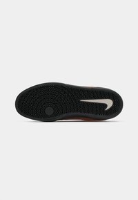 Sola de sapato de borracha com um padrão de piso em zigue-zague. Predominantemente preta com um logo Nike em cinza. Apresenta um ponto de tração redondo no centro.