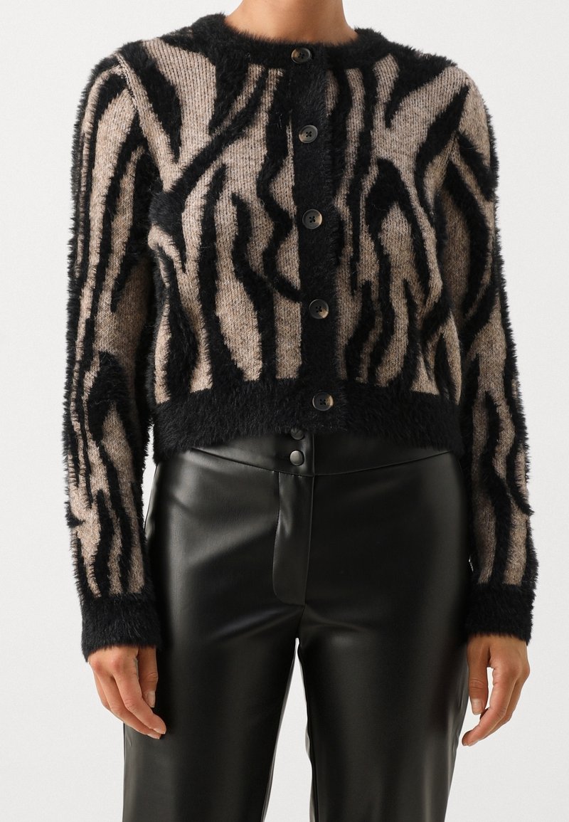 Cardigan duveteux boutonné avec des rayures zèbre abstraites beige et noir, porté avec un pantalon en cuir noir taille haute.