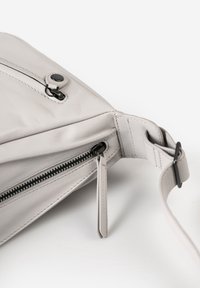 Grijze leren tas met een gladde textuur, voorzien van een zwarte ritssluiting en hardware, een plat ontwerp en een hengsel om te dragen.
