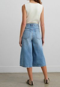 Pantalones culotes de mezclilla azul claro de cintura alta con un acabado desvanecido, dobladillo deshilachado y dos bolsillos traseros, combinados con zapatos negros de tejido sin cordones.