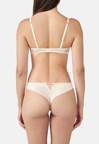 Set di lingerie beige con reggiseno senza cuciture e dettagli in pizzo, completo di g-string coordinato; texture liscia simile alla seta.