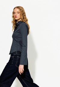 Granatowa koszula z długimi rękawami i ostrym kołnierzem, o dopasowanym kroju i gładkiej fakturze, zestawiona z ciemnymi dżinsami z białymi szwami.