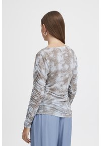 Långärmad topp i ljusblått med ett brunt ormmönster, med rynkade sidor för textur och en rund halsringning. Mjukt tyg.