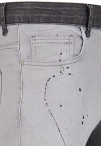 Grå denimjeans med en kontrastfarge i svart på midjen, med malingssprutdetaljer på venstre lår og standard baklommelys.