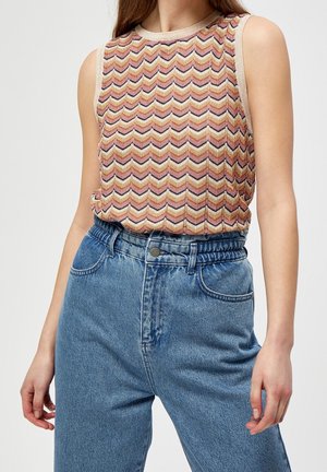 Wzorzysty bezrękawnik z motywem jodełki w kolorach różowym, złotym i kremowym, zestawiony z niebieskimi dżinsami z wysokim stanem.