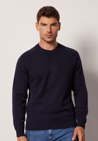 Marinblå crew-neck tröja gjord av mjukt strikkat tyg. Har ribbade ärmslut och nederkant, med en slät yta och insydd axeldesign.