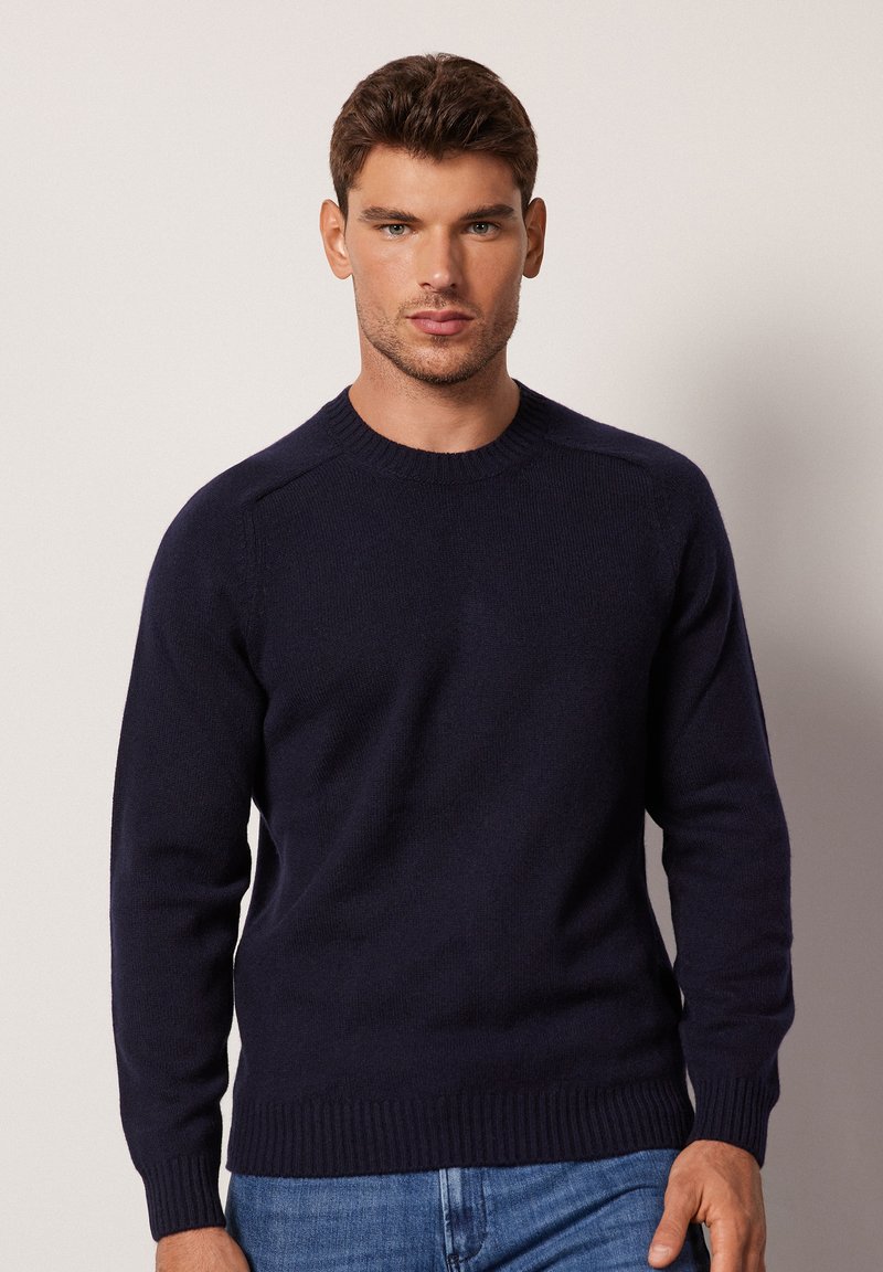 Marinblå crew-neck tröja gjord av mjukt strikkat tyg. Har ribbade ärmslut och nederkant, med en slät yta och insydd axeldesign.