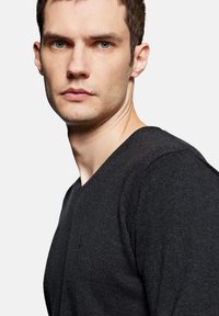 Czarny sweter z dekoltem w kształcie V wykonany z dzianiny, z dopasowanym krojem i subtelnymi detalami szycia, noszony przez modelkę o jasnej karnacji.