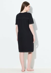 Sort kjole med korte ærmer og afslappet pasform, med en samlet rygdesign og kontrasterende syninger langs halsen og kanten. Blødt stof.