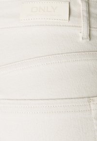 Tissu en denim blanc avec des détails de couture visibles. Présente une étiquette avec le texte "ONLY". La texture semble lisse et douce.