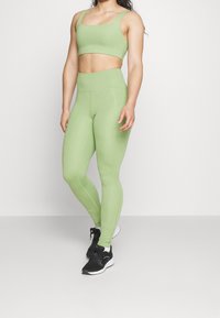 Jasnozielony stanik sportowy oraz legginsy o wysokim stanie wykonane z elastycznego materiału. Legginsy mają gładką fakturę i dopasowany krój.