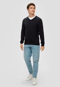 Czarny sweter z dekoltem w serek i długimi rękawami, zestawiony z jasnoniebieskimi dżinsami i białymi sneakersami. Prosty design, gładka tekstura, brak widocznych wzorów.