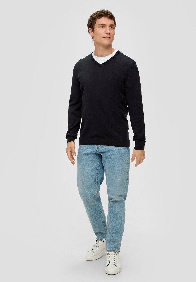 Zwarte V-hals trui met lange mouwen, gecombineerd met lichtblauwe jeans en witte sneakers. Eenvoudig ontwerp, gladde textuur, geen opvallende patronen.