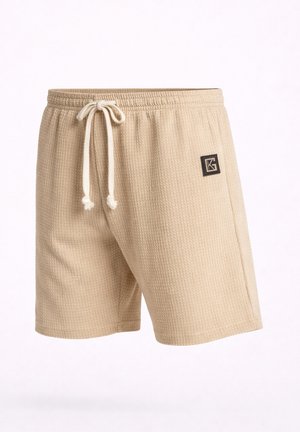 Pantaloncini beige in maglia strutturata con vita elastica e coulisse bianca, caratterizzati da una piccola toppa con logo nero sulla coscia destra.