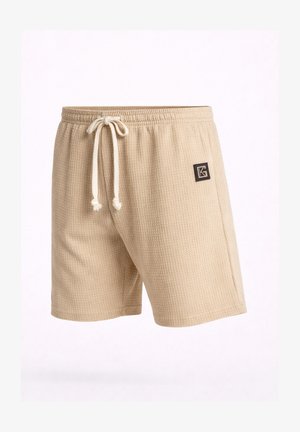 Pantaloncini beige in maglia strutturata con vita elastica e coulisse bianca, caratterizzati da una piccola toppa con logo nero sulla coscia destra.