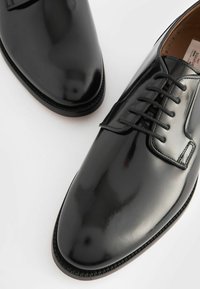 Chaussures en cuir noir avec une finition brillante, bout rond et lacets plats. Présentent un bord cousu et une doublure intérieure beige.