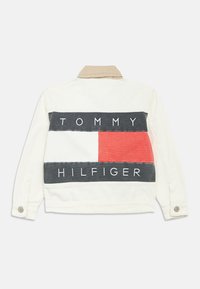 Biela denimová bunda s béžovým golierom. Na zadnej strane je veľká grafika s nápisom "TOMMY HILFIGER" tučnými písmenami a panelmi v červenej, bielej a námorníckej modrej farbe.
