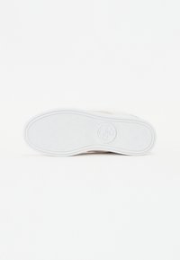 Vit sneakersula med en texturerad yta och en cirkulär logotyp i mitten. Enkel, ren design med minimal detaljer.