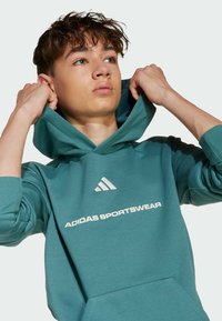 Turkos Adidas hoodie med kenguruficka, ribbade muddar och vit logotext, med en avslappnad passform och mjuk textur.