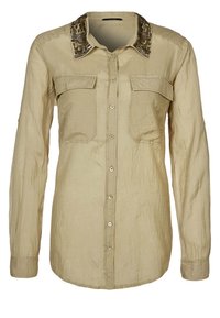 Camisa beige de manga larga con dos bolsillos en el pecho, tejido texturizado y cuello estampado. Presenta cierres de botón en la parte delantera.