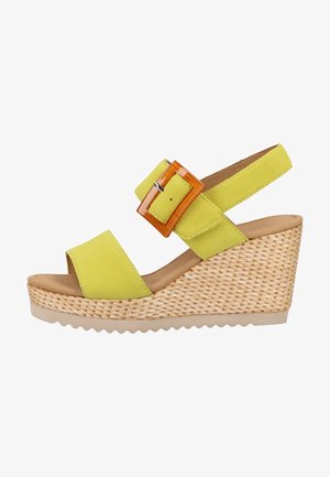 Sandalia de cuña de ante amarillo con punta redondeada abierta, correa ajustable en el tobillo y una hebilla decorativa naranja. Tacón con textura tejida y suela de goma.