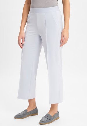 Helle graue, dehnbare Stoffhosen mit flacem Bund, weiten Beinen und dezenten Seitennähten, kombiniert mit grauen Slippern.