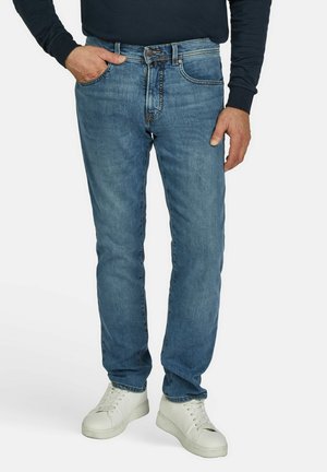 Blaue Denim-Jeans mit schmalem Schnitt, klassischem Fünf-Taschen-Design und subtilen Ausbleichungen. Getragen mit weißen Sneakers.