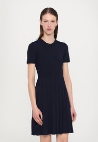 Navy blue ribbed dress with short sleeves, fitted bodice, and a pleated skirt. Smooth texture, round neckline, and knee-length design.