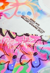 T-shirt colorée en tissu doux, ornée d'un motif floral avec des tons roses et bleus, ainsi que d'un texte concernant une exposition d'art.