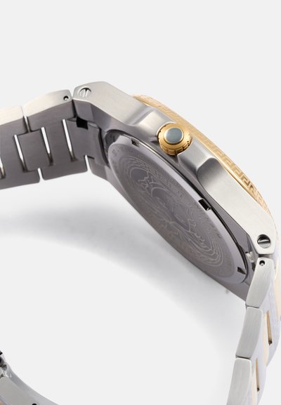 Orologio con finitura argento e oro, dotato di una lunetta oro texturizzata, bracciale in acciaio inox e cassa rotonda. Dettagli notevoli includono una corona rotonda e un fondello incavato.