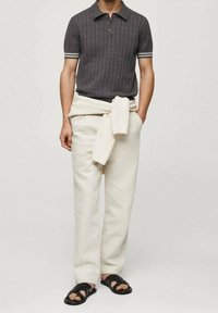 Polo shirt en charbon à côtes avec patte de boutonnage à trois boutons, manches à rayures blanches ; pantalon crème ; sweater en tricot léger noué à la taille ; sandales noires.