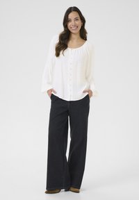 White textured blouse with buttons, loose fit, and long sleeves paired with high-waisted black wide-leg jeans. Dry texture, neutral colors.