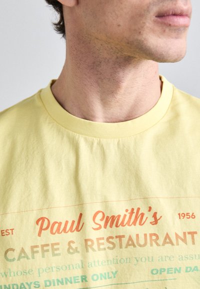 Yellow cotton t-shirt featuring multicolored text: "Paul Smith's Caffe & Restaurant" with a vintage design. Crew neck, relaxed fit.