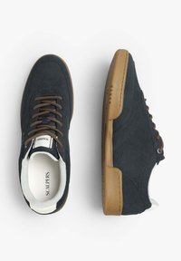 Zapatillas de gamuza azul con cordones marrones, suelas de goma y acentos blancos. Presentan una puntera perforada y una etiqueta con el logo en la lengüeta.