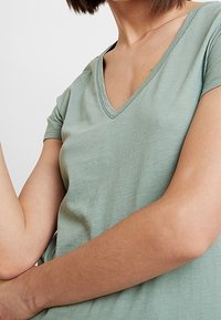 Ljusgrön t-shirt med v-ringning, tillverkad av mjukt och lätt tyg. Korta ärmar och en avslappnad passform, med minimal textur och detalj.