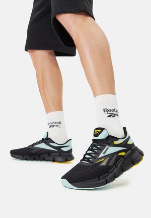 Czarne buty do biegania z siateczkową cholewką, jasnoniebieskimi akcentami, żółtymi detalami i grubą podeszwą. W połączeniu z białymi skarpetkami Reebok.