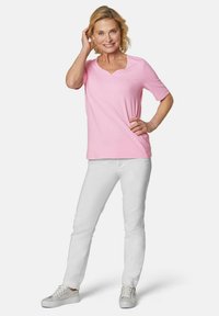 Rosa Kurzarm-T-Shirt mit V-Ausschnitt und dezenten Verzierungen, kombiniert mit weißen Hosen und hellen Sneakers. Glatter, lässiger Stoff.