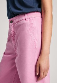 Calças de algodão cor-de-rosa com uma textura suave, apresentando bolsos laterais, detalhes cosidos e um botão de metal na cintura.