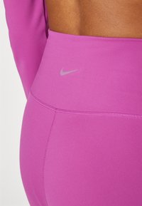 Roza visoka športna legging hlače z gladkim, raztegljivim materialom. Imajo subtilen sivi Nike logotip in ravne šive za udobje.
