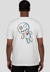 Camiseta blanca con un gráfico colorido de una muñeca estilizada con cabeza de calavera y un diseño de corazón en la parte posterior. Mangas cortas, tejido suave.