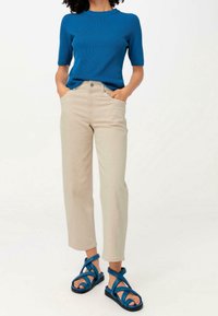 Ljusbeige byxor med hög midja, kort blå ribbad topp och blå sandaler med korsband. Har en avslappnad passform och texturerat tyg.