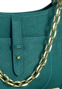 Tegelkleurige leren handtas met een getextureerd oppervlak, gouden kettingbandjes en een centrale klep met een sluiting met studs.