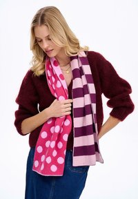 Fleecový šál s ružovou farbou so bielymi bodkami a ružovým pruhovaným vzorom, ktorý zdôrazňuje mäkkú textúru a výrazný farebný kontrast.