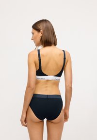 Czarny stanik i majtki z wysokim stanem z białą taśmą Calvin Klein. Materiał wydaje się miękki; design charakteryzuje się regulowanymi ramiączkami i bezszwowym wykończeniem.