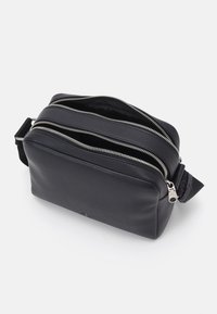 Neceser de cuero negro con doble cremallera, forma rectangular, superficie texturada y un asa lateral para facilitar el transporte.