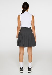 Canottiera bianca senza maniche abbinata a una gonna plissettata grigia scura. L'outfit ha una vita aderente ed è completato da calze bianche e scarpe sportive.