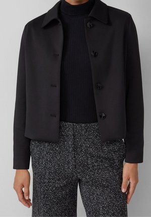 Black buttoned jacket over black ribbed turtleneck, paired with black and white herringbone patterned pants, shown from shoulders to hips.