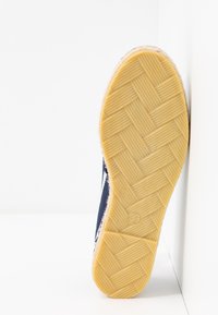 Marinblå tygskosula med en texturerad gul gummibotten, med en fiskbensmönster och storleksmärke 39. Kantad med trim av naturliga fibrer.