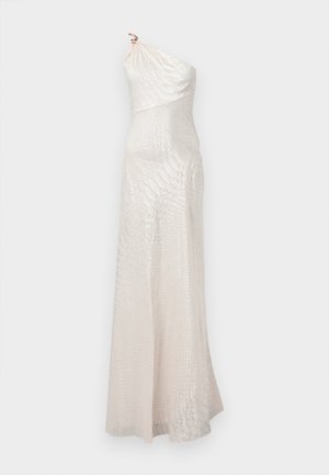 Noor naine seisab käsi puusal, kandes ühele õlale langevat valget tekstuuriga maksikleiti, millel on kuldne õlaklamber.